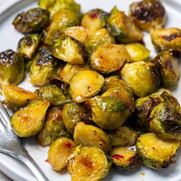Roasted Brussels sprouts on a white plate, crispy and seasoned; healthy vegetable side dish, perfect for clean eating, weight loss, and nutritious meals.