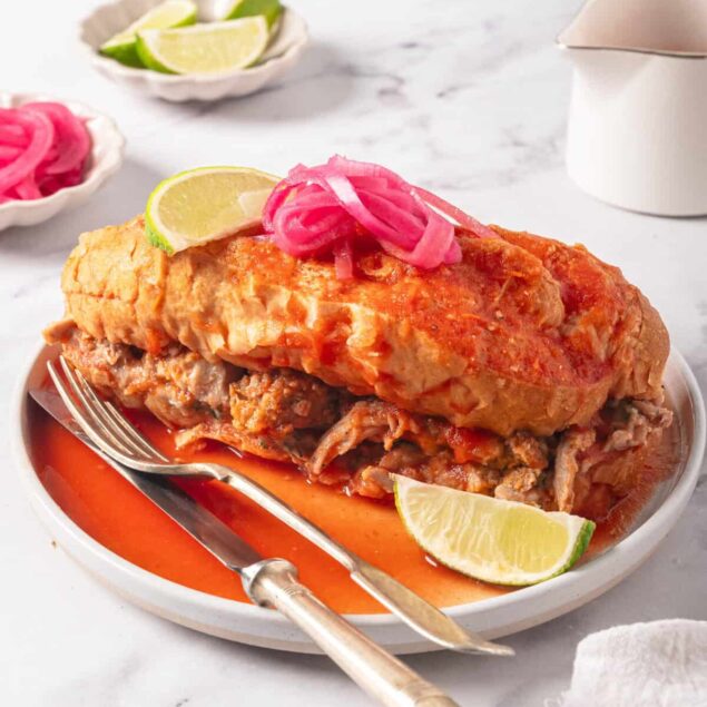 Succulent Mexican chicken tortilla soup with vibrant red broth, garnished with lime wedges and pickled red onions, served on a white plate. Perfect for healthy meal ideas and comfort food lovers.