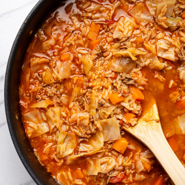 Hearty homemade vegetable and ground beef soup in a black skillet with a wooden spoon, perfect for healthy, nutritious meals.