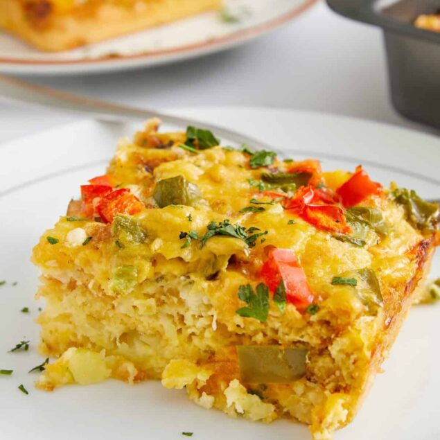 Vegetable casserole with melted cheese, fresh herbs, and colorful bell peppers on a white plate. Healthy, easy-to-make meal perfect for meal prep and diet-conscious cooking.