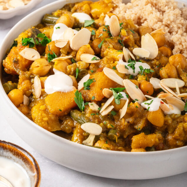 Savory chickpea and vegetable curry garnished with sliced almonds and fresh herbs, served alongside fluffy couscous, perfect for healthy, plant-based meal recipes.