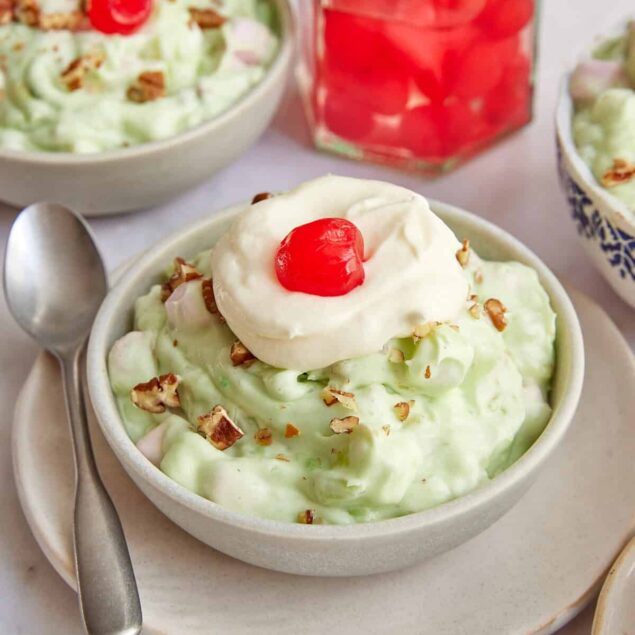 Creamy cherry pudding with whipped topping, chopped nuts, and maraschino cherries in a white bowl, served on a white plate with a silver spoon for a healthy dessert option.