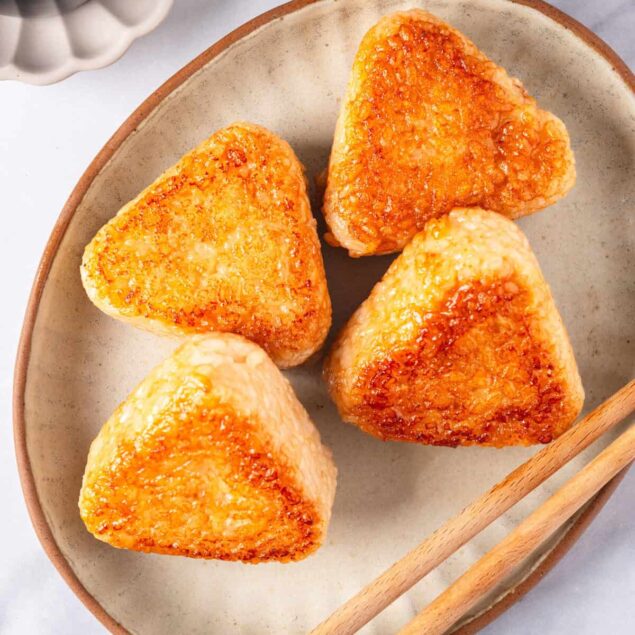Crispy baked cauliflower tots on a beige plate, skewers on the side, healthy vegetarian snack, served on marble surface, food photography for nutritious meal ideas.