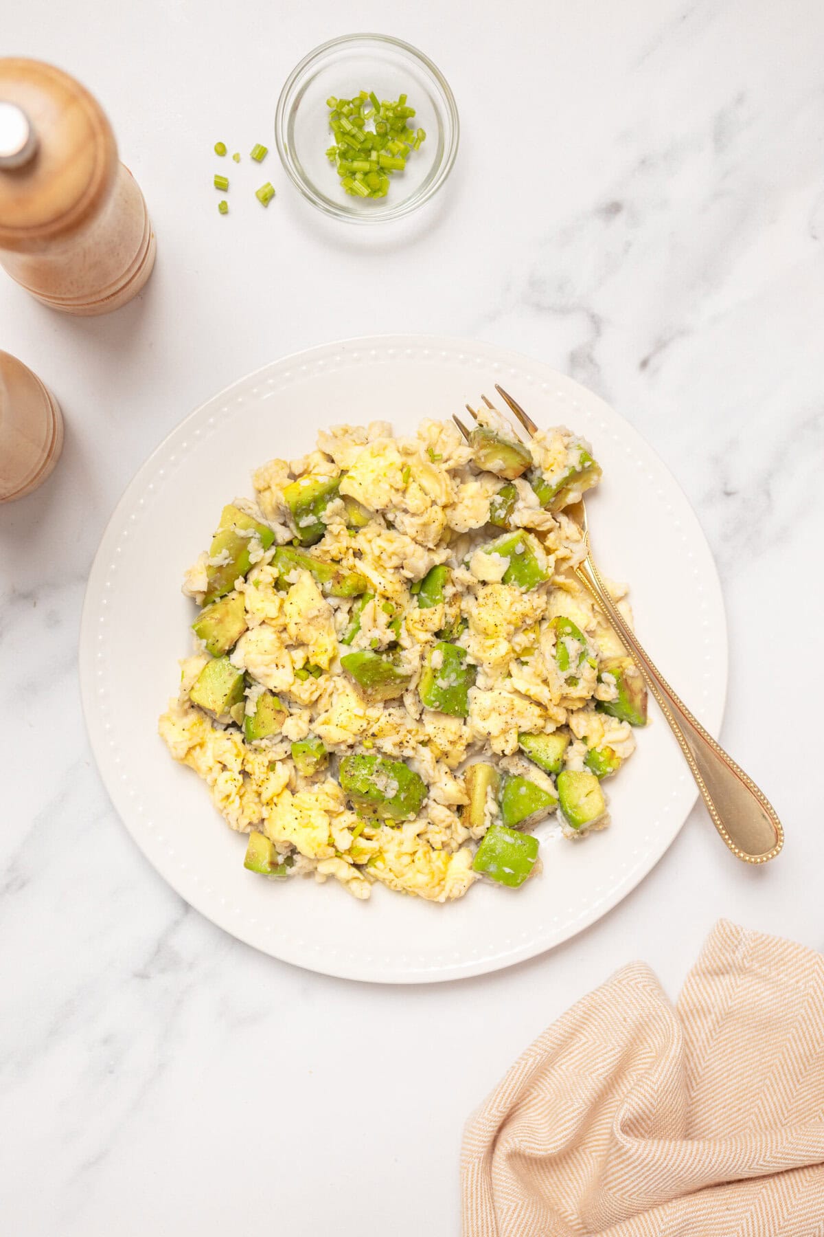 Scrambled eggs with chopped green avocado on a white plate, healthy breakfast recipe from Food Faith Fitness featuring nutritious ingredients for a balanced diet.