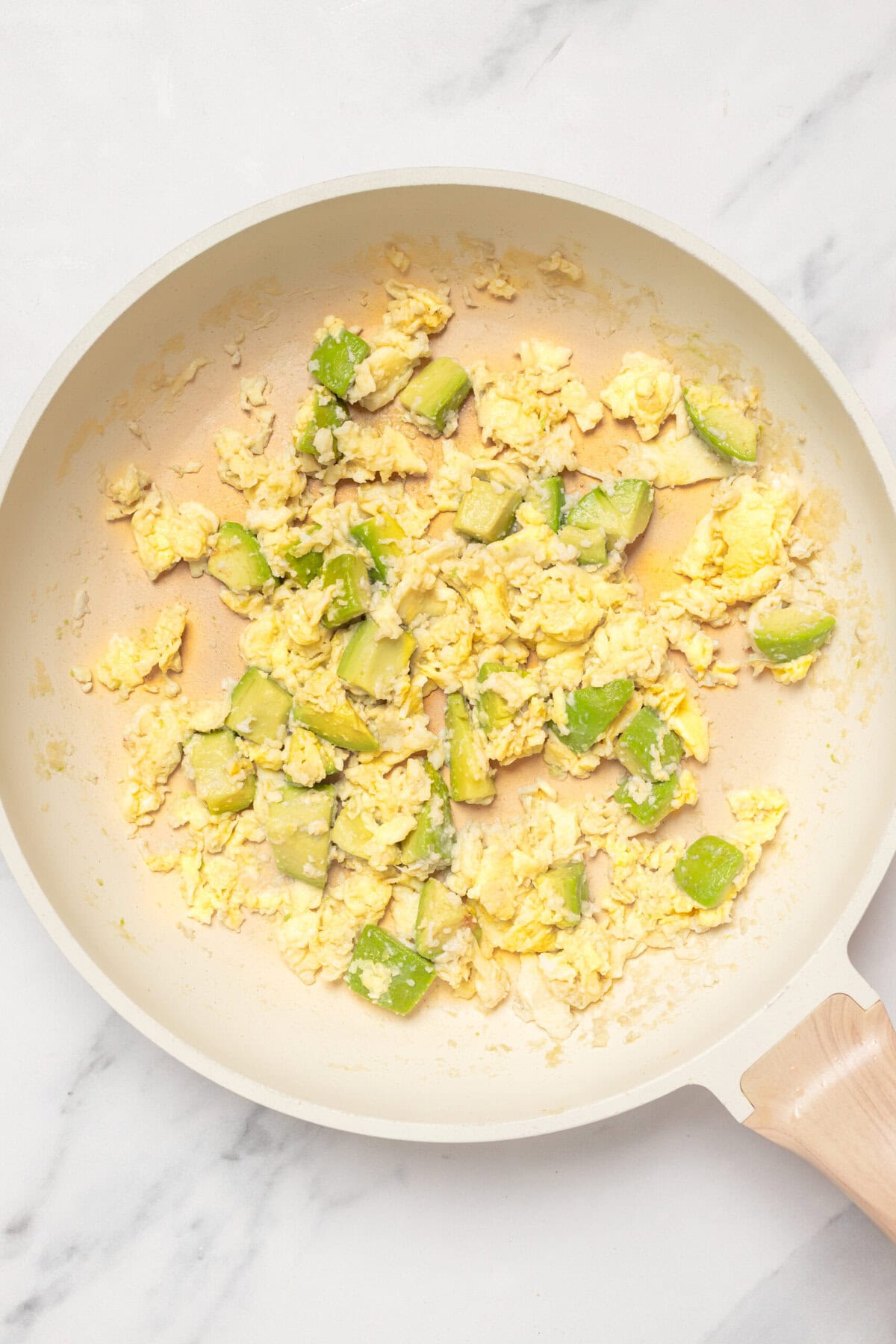 Scrambled eggs with chopped green zucchini in a white non-stick skillet for healthy breakfast.