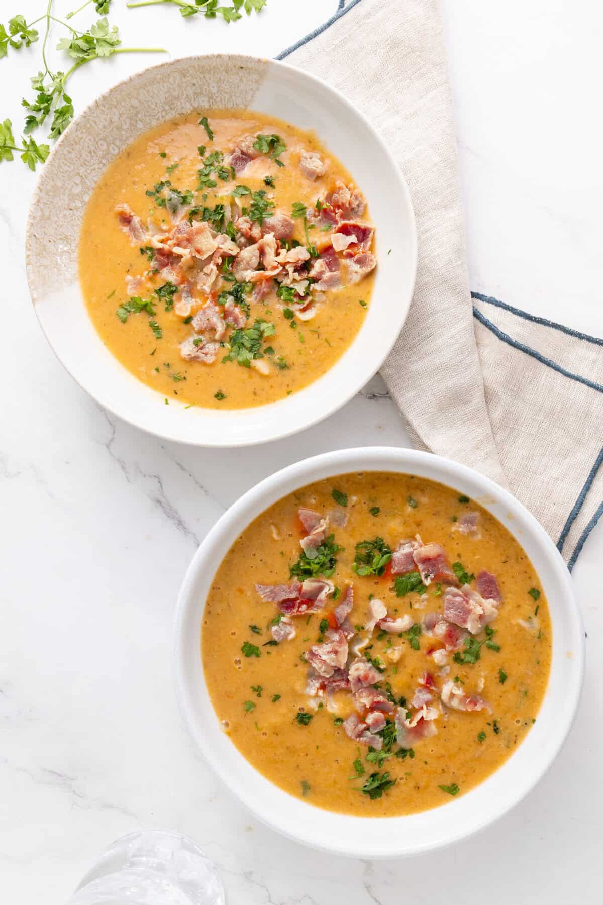 Creamy bacon and herb potato soup served in white bowls, garnished with chopped parsley. Perfect for healthy, comforting meals, featuring fresh ingredients and rich flavors. Food Faith Fitness recipe.