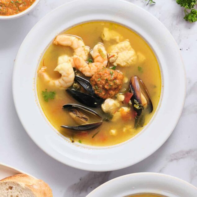 Seafood vegetable soup with shrimp, mussels, and fish in a flavorful broth, served with fresh bread on a white background, highlighting healthy, delicious, nutritious recipes.