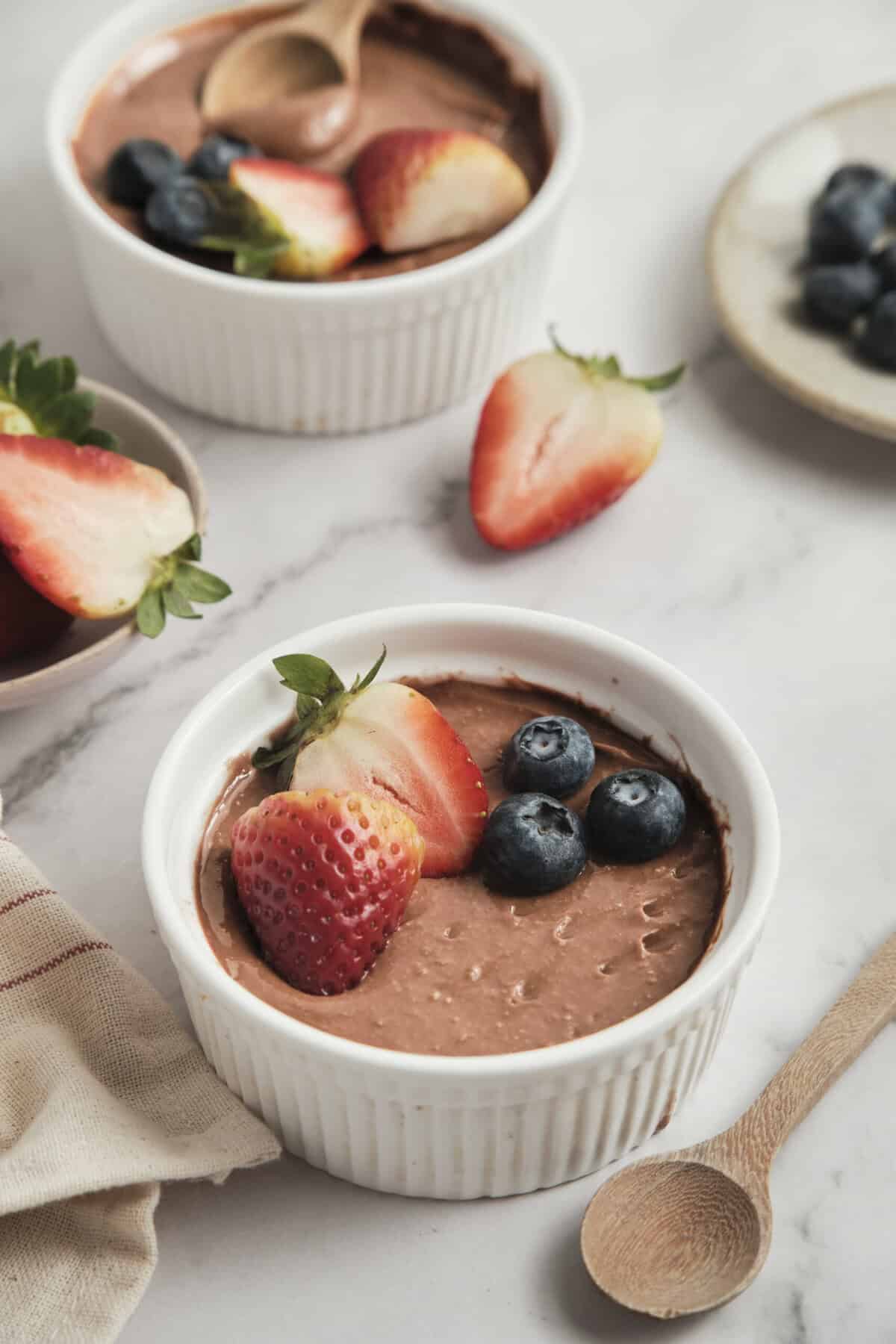 Creamy chocolate avocado pudding topped with fresh strawberries and blueberries, perfect healthy dessert for food and fitness enthusiasts.