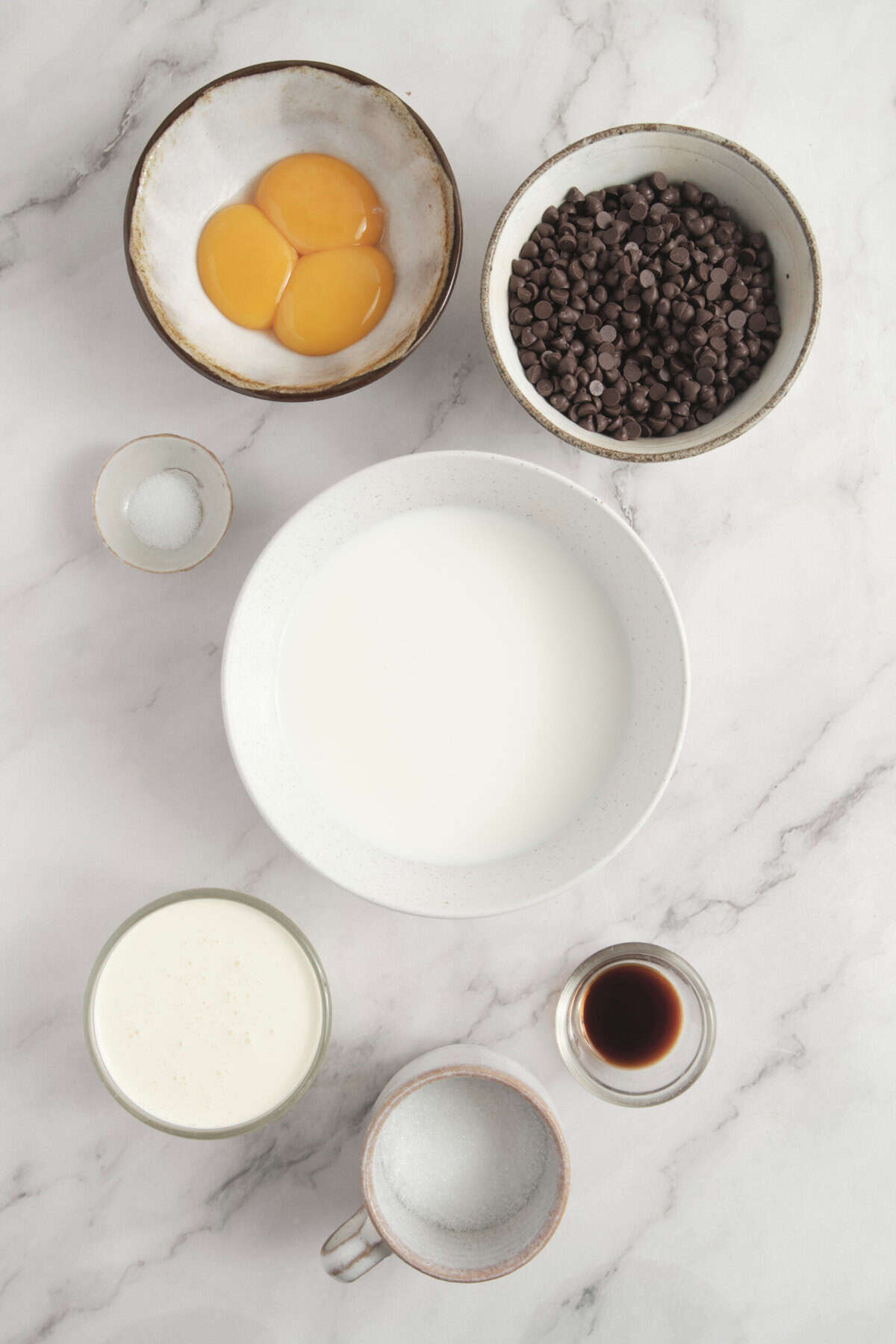 Eggs, chocolate chips, milk, vanilla, and sugar on a marble surface, ingredients for healthy baking recipes from Food Faith Fitness.