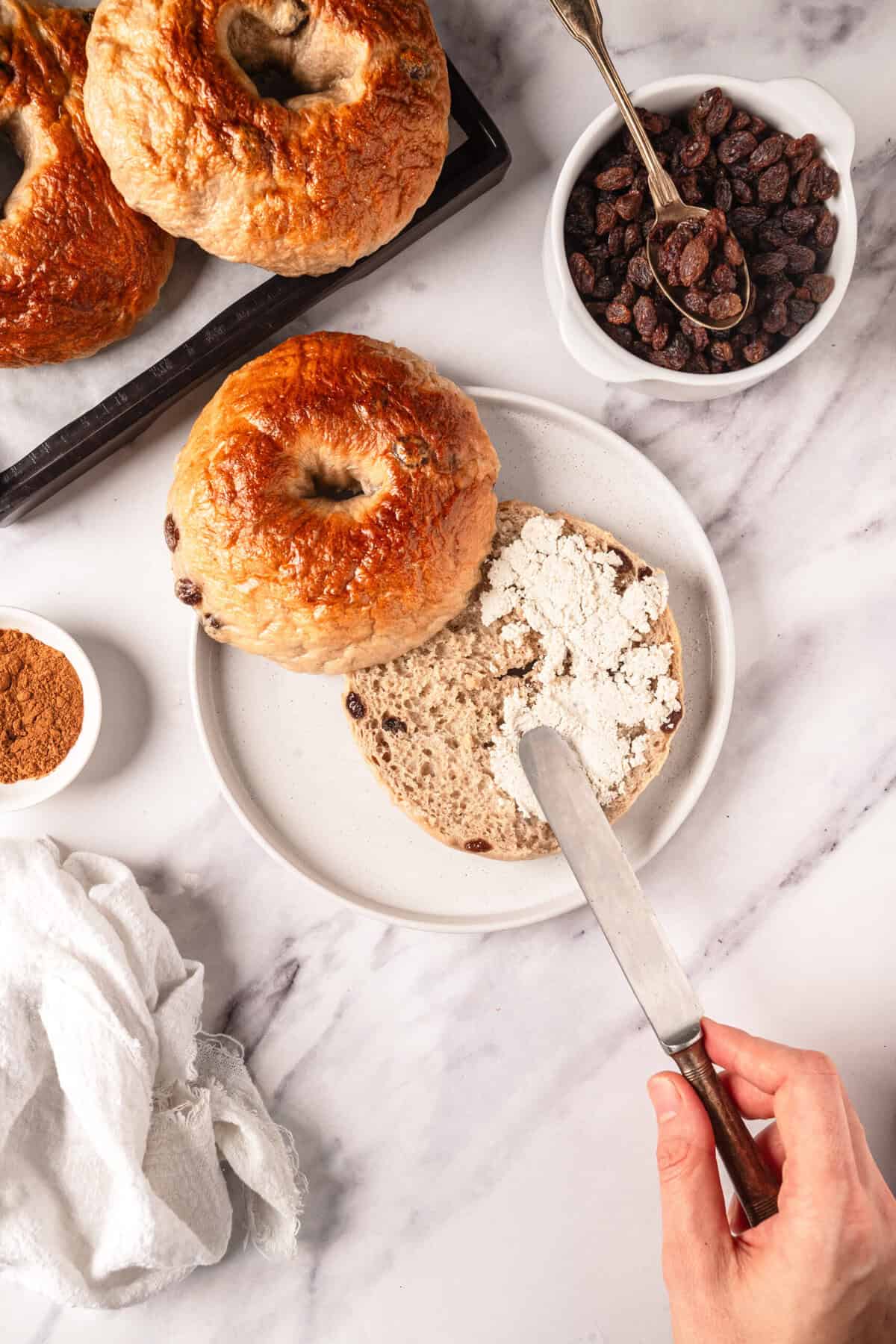 Buttermilk bagels with oats, raisins, and cinnamon on a white marble surface, organic ingredients for healthy breakfast, Food Faith Fitness bread recipe, clean eating, homemade bagels preparation.