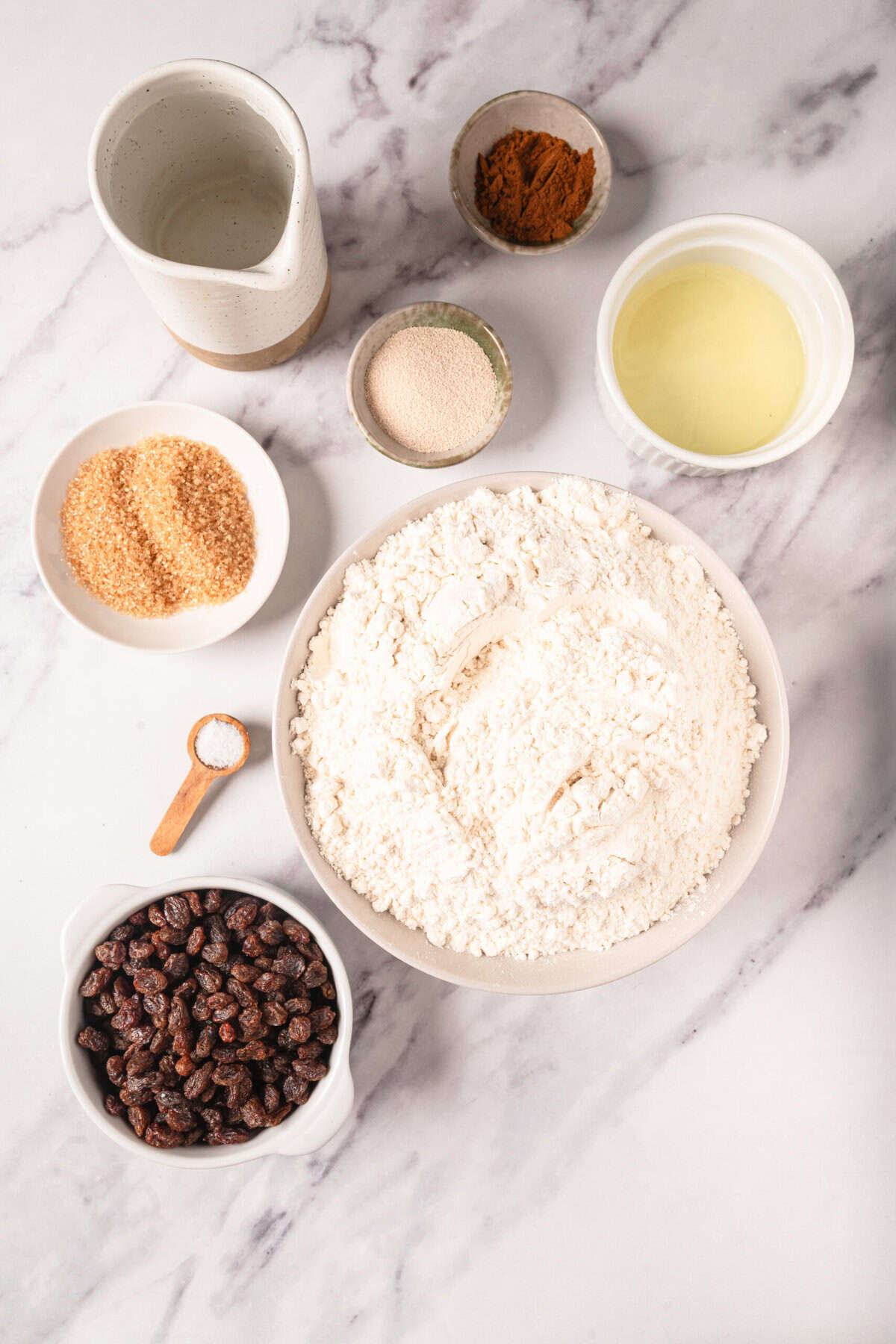Cream cheese, flour, dried cranberries, brown sugar, cinnamon, vanilla extract, and almond milk on marble surface for healthy baking recipes.