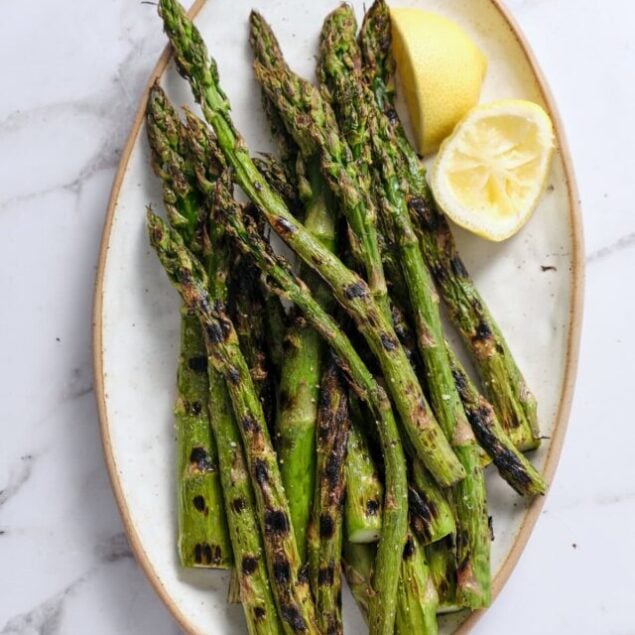 Grilled asparagus with lemon wedges on a white plate, healthy vegetable side dish from Food Faith Fitness recipe collection.