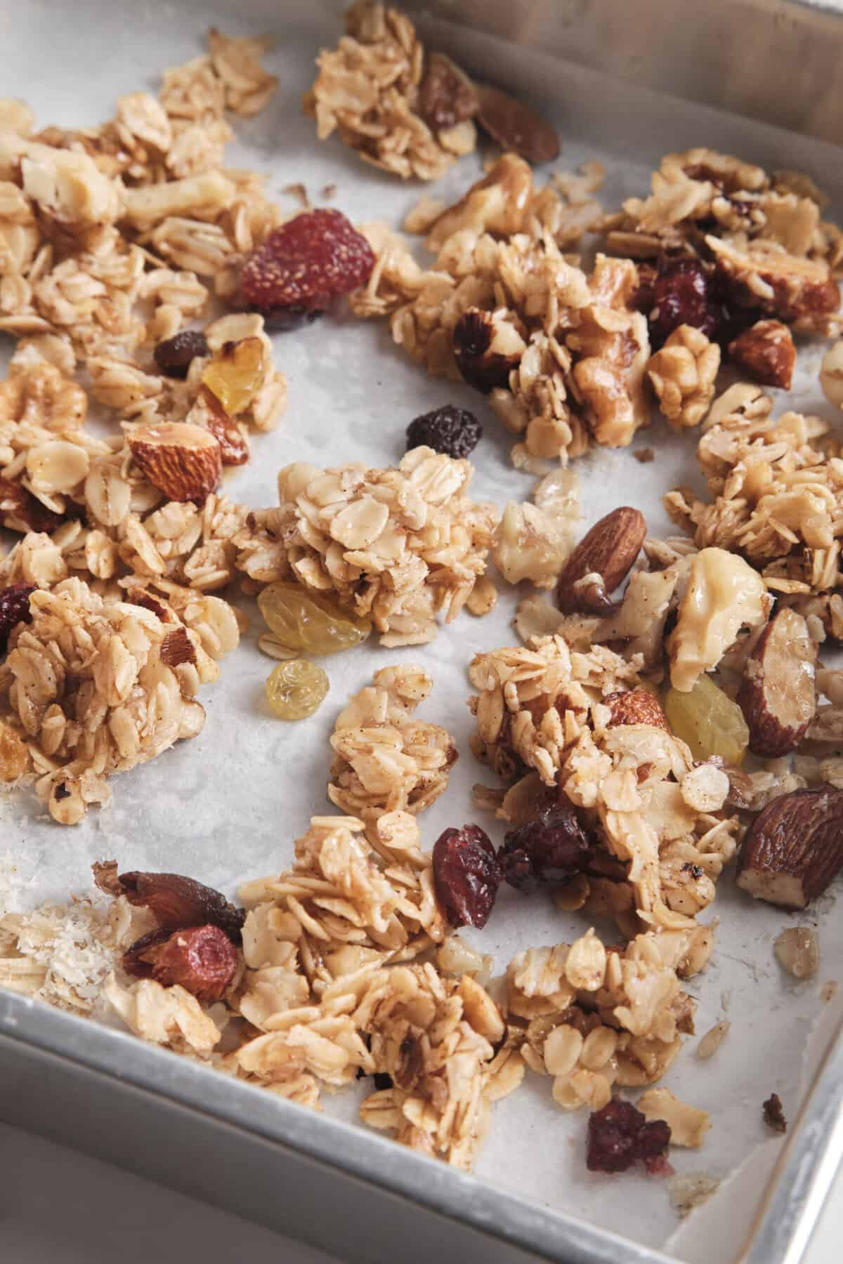 Homemade granola clusters with oats, nuts, and dried fruits on baking sheet, healthy snack option, gluten-free, nutritious, easy to make recipe from Food Faith Fitness.