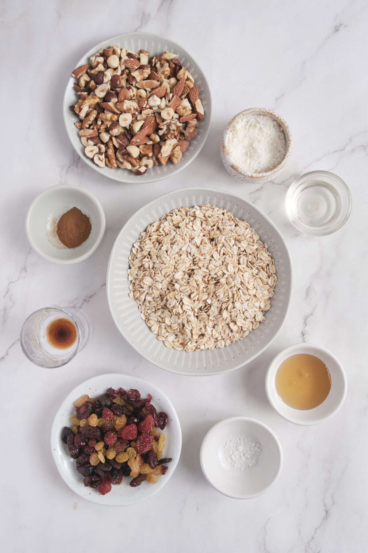 Meal prep ingredients for oatmeal topped with mixed dried berries, chopped nuts, honey, and spices on a white marble surface. Healthy breakfast ideas for weight loss and fitness.