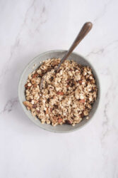 Roasted granola in a light ceramic bowl with a spoon, perfect for healthy eating and fitness meal prep.