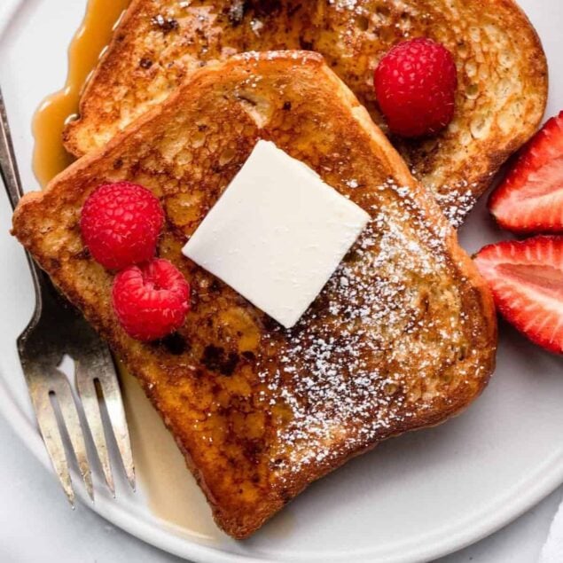 Butter-french-toast-with-berries-and-syrup-on-white-plate.