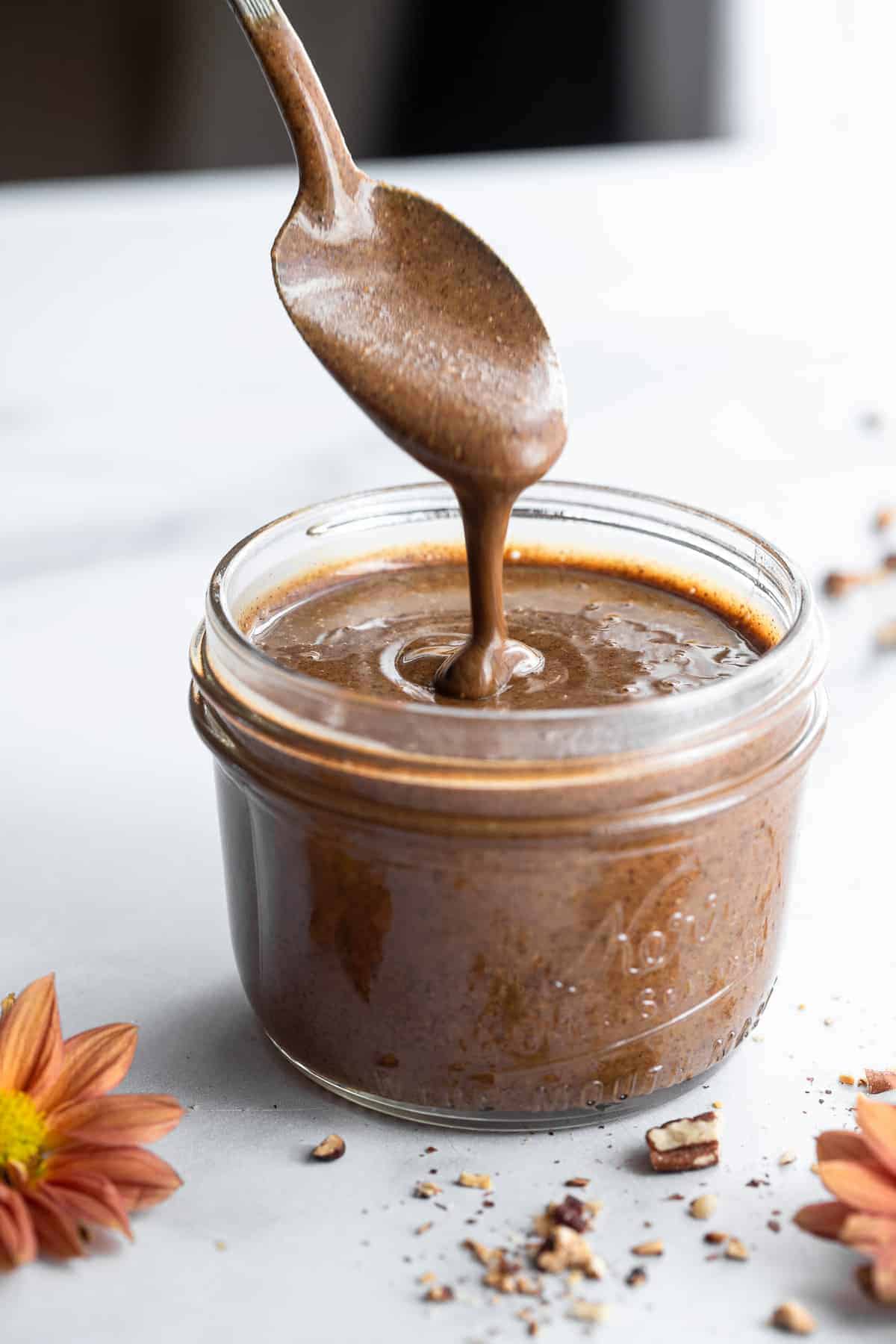 a spoon dripping homemade pecan butter into a glass jar