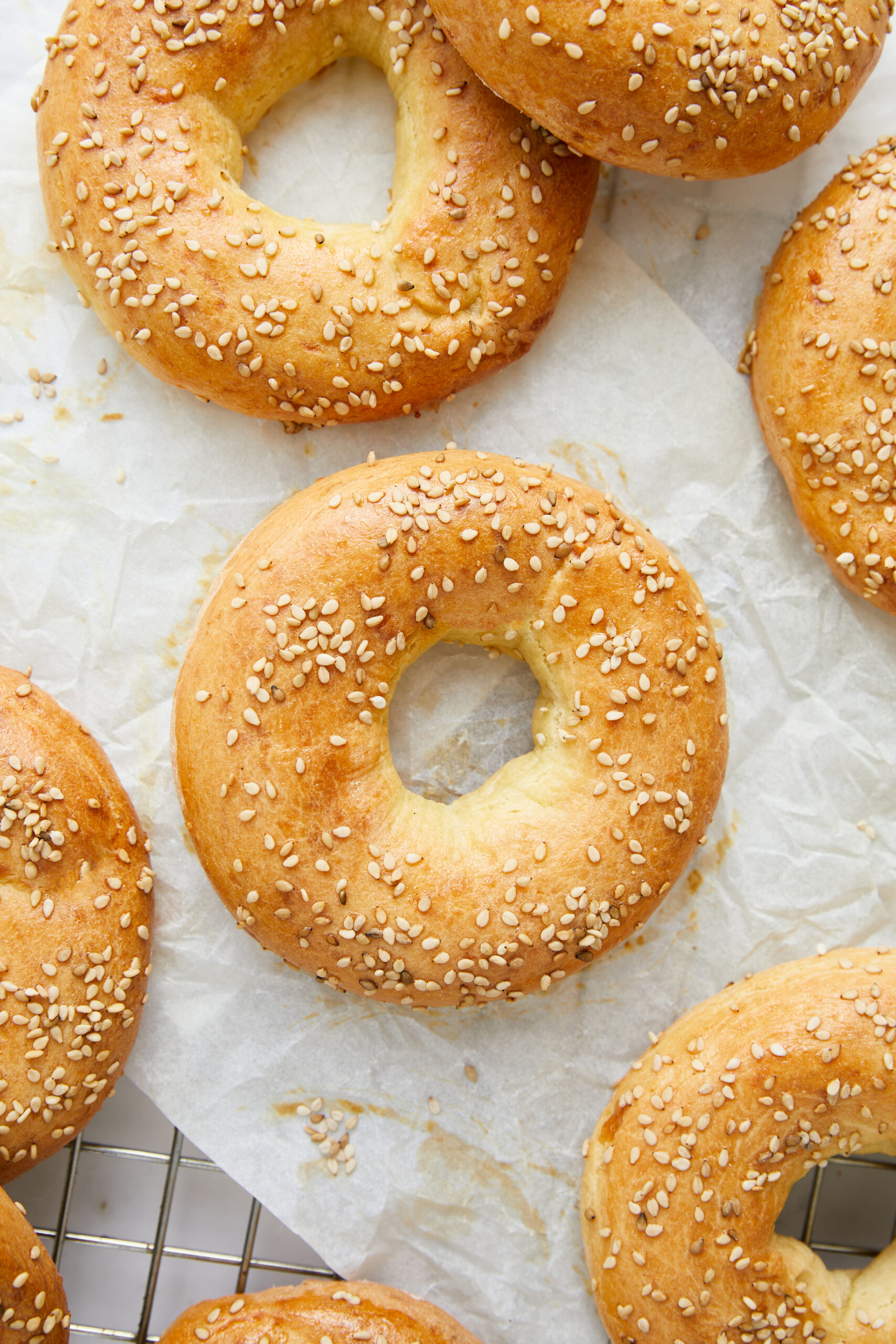 Freshly baked sesame bagels on parchment paper, showcasing golden crust and sesame seed topping, perfect for breakfast or snacking.