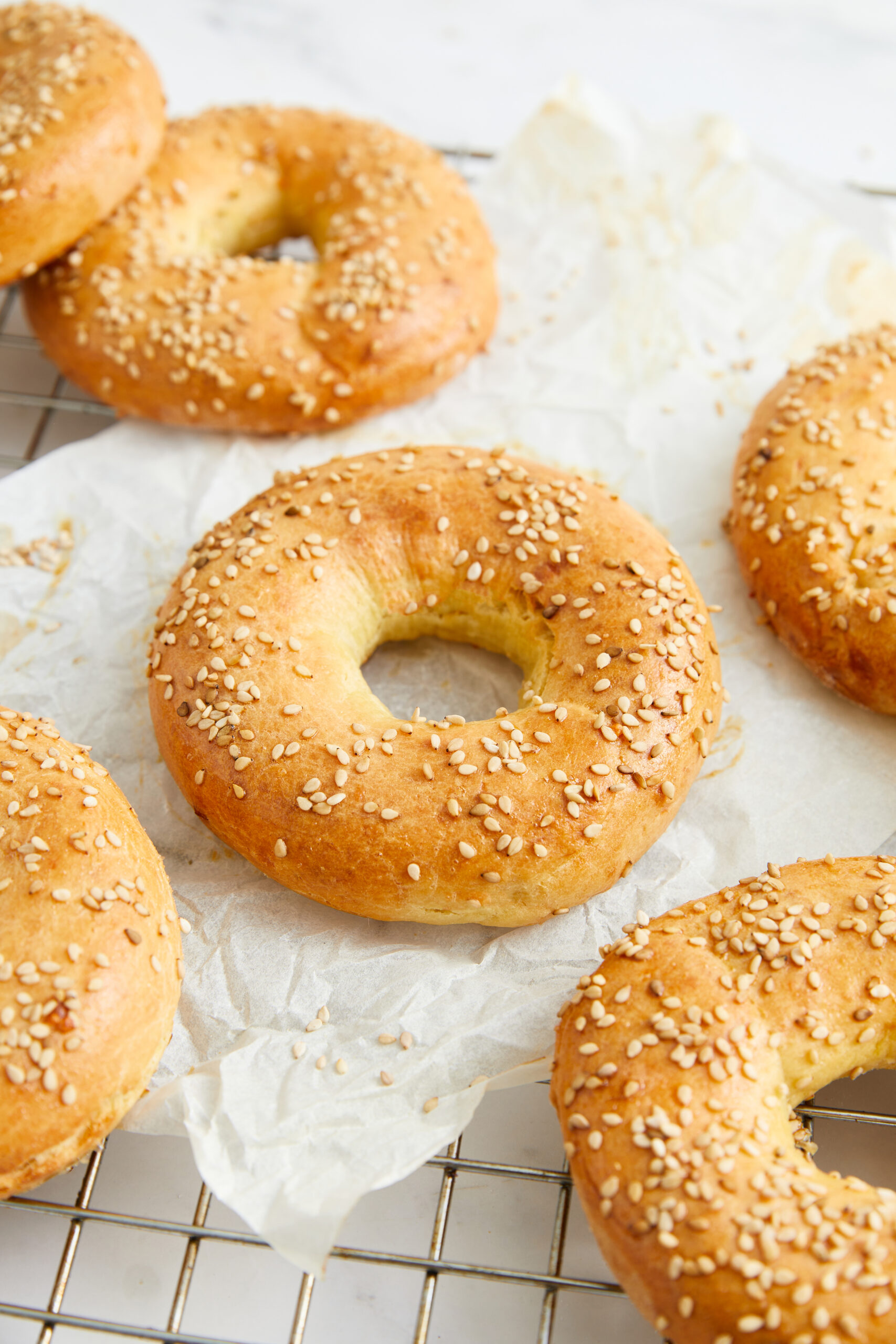 Soft baked bagels with sesame seeds on top, fresh from the oven, on a wire cooling rack. Perfect for a healthy breakfast or snack, featuring gluten-free and whole-grain options.