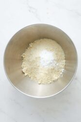 Finely ground almond flour and baking powder in a metal mixing bowl, ready for a healthy recipe at Food Faith Fitness.