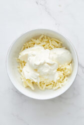 Cream cheese, shredded cheese, and sour cream in a white bowl, ready for healthy cheese dip or spread, emphasizing nutritious recipes and snack ideas from Food Faith Fitness.