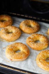Soft homemade bagels topped with sesame seeds, baking on parchment paper in a home oven. Perfect for healthy breakfast recipes and nutritious eating. Freshly baked, golden, and delicious.