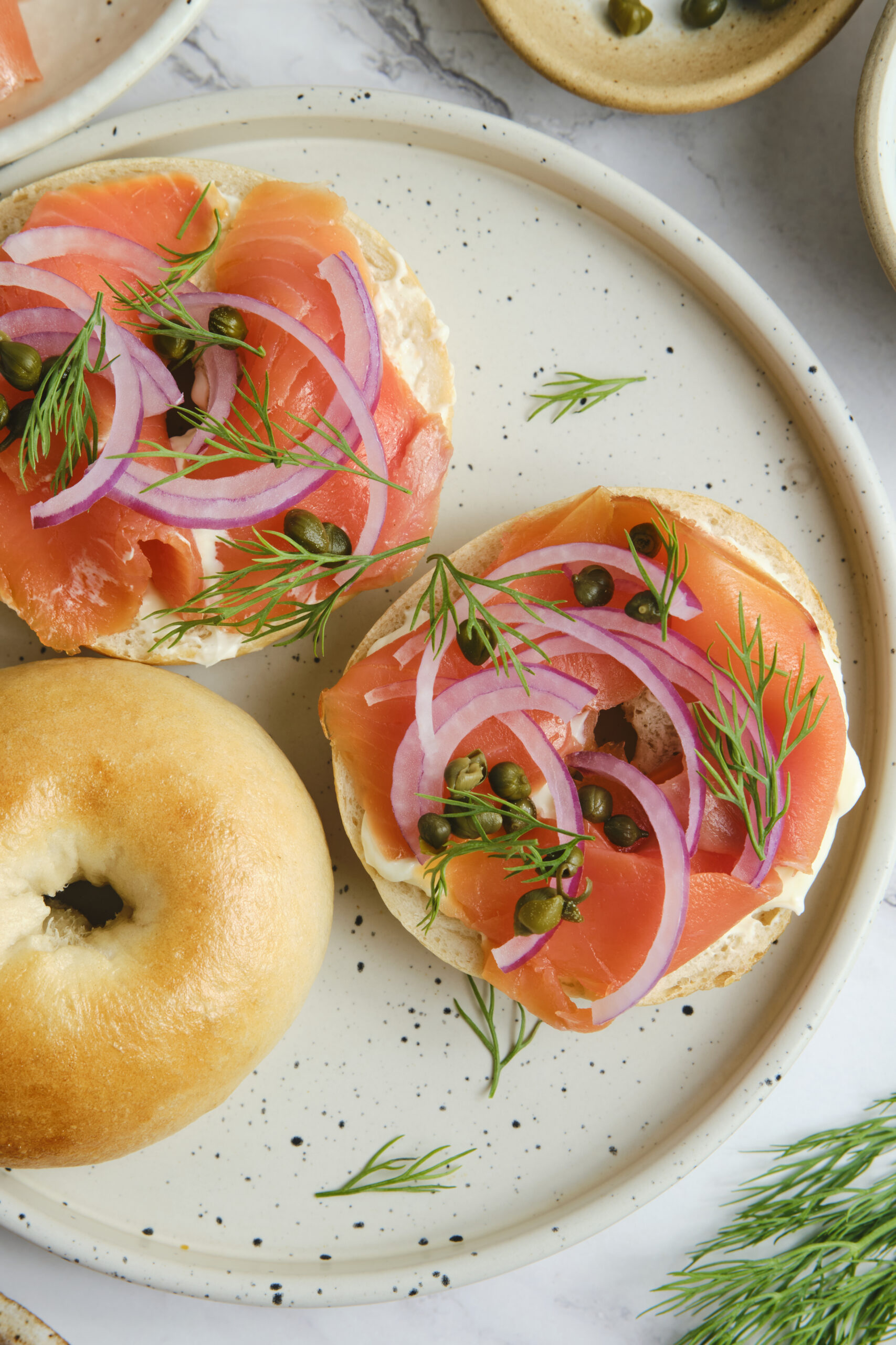 Fresh smoked salmon bagel bites topped with red onion, dill, and capers, served on a white ceramic plate for a healthy breakfast or snack.