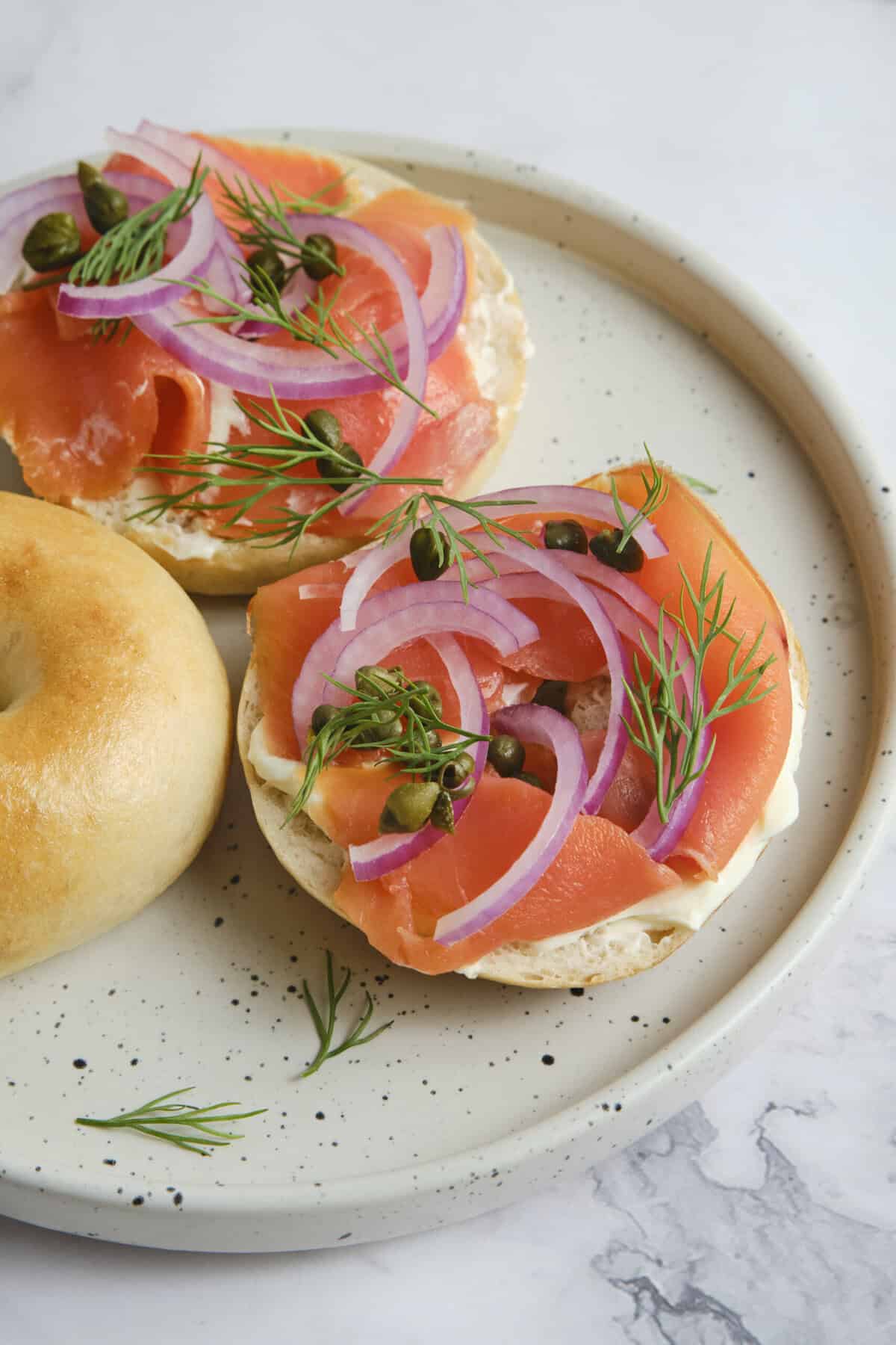 Smoked salmon bagel with red onions, capers, and fresh dill on a white plate, emphasizing healthy protein-rich breakfast options and balanced meal ideas for fitness and wellness.