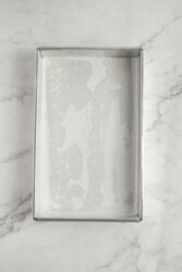 Empty baking tray lined with parchment paper on a marble countertop.