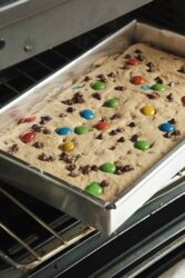 Chocolate chip cookie bar with colorful M&M candies baking in an oven tray.