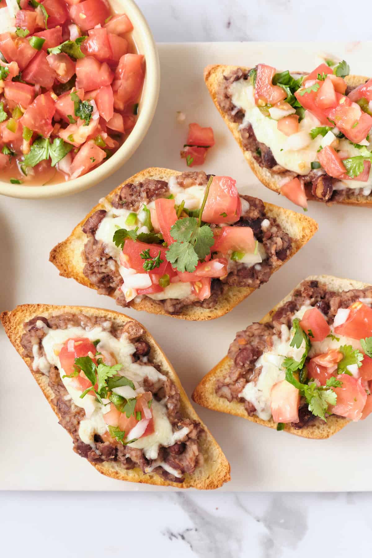 Savory beef taco bites with queso, topped with pico de gallo and cilantro, served on a white platter with fresh tomato salsa in a bowl.