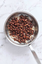 Cooked black beans with chopped onions in a stainless steel skillet, healthy vegetarian meal, high-protein plant-based food, nutritious ingredients for meal prep.