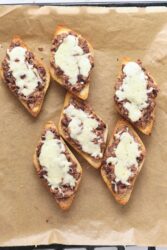 Creamed beef and mushroom toast with melted cheese on toasted bread slices, served on a parchment baking sheet.