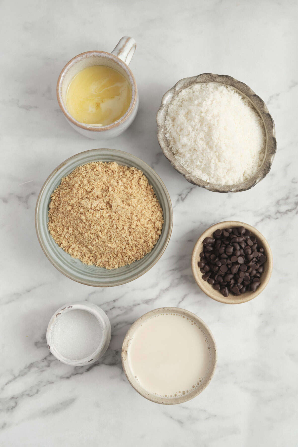 Creamy melted butter in a mug, coconut flour, shredded coconut, chocolate chips, and almond milk arranged on a marble surface for healthy baking with a focus on wholesome ingredients. | Easy healthy baking ingredients: butter, coconut flour, shredded coconut, chocolate chips, almond milk on marble surface | An overhead shot of essential ingredients for healthy baking, including butter, coconut flour, shredded coconut, chocolate chips, and almond milk, perfect for nutritious recipes from Food Faith Fitness. | The image showcases key ingredients used in healthy baking recipes such as coconut flour, shredded coconut, chocolate chips, and almond milk, all arranged neatly on a marble countertop from Food Faith Fitness. |.