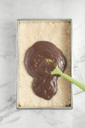 Creamy chocolate layer spreading over a crumb crust in a baking pan.