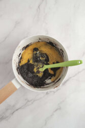 Cream mixture with cookie crumbs in a bowl, with a green spatula on a white marble surface.