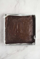 Decadent homemade chocolate cake with creamy frosting in a square pan on a marble surface. Perfect for healthy dessert recipes and indulgent treats from Food Faith Fitness.