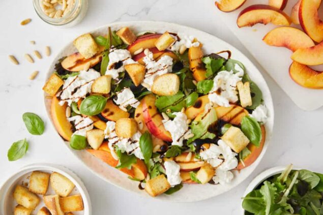 Fresh peach salad with mixed greens, croutons, feta cheese, sunflower seeds, and balsamic drizzle - healthy and delicious summer meal.