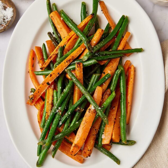 Roasted carrot and green bean vegetable stir-fry with black pepper and sea salt on a white oval plate, healthy plant-based meal, food recipe from Food Faith Fitness.