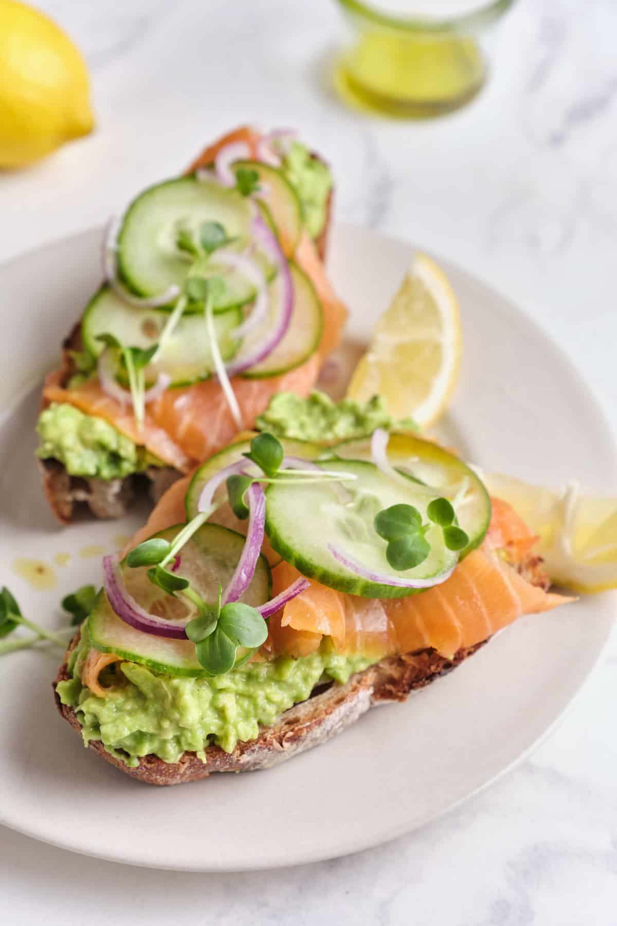 Fresh smoked salmon toast with avocado, cucumber, red onion, microgreens, and lemon on whole-grain bread, healthy and delicious recipes from Food Faith Fitness.