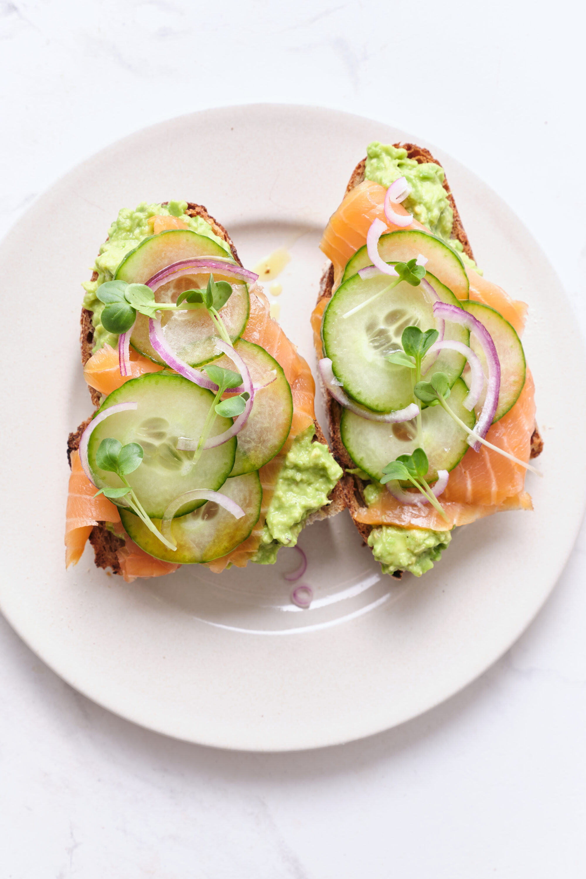 Sourdough avocado smoked salmon toast with cucumber, red onion, and microgreens on white plate, healthy eating, and nutritious breakfast idea.