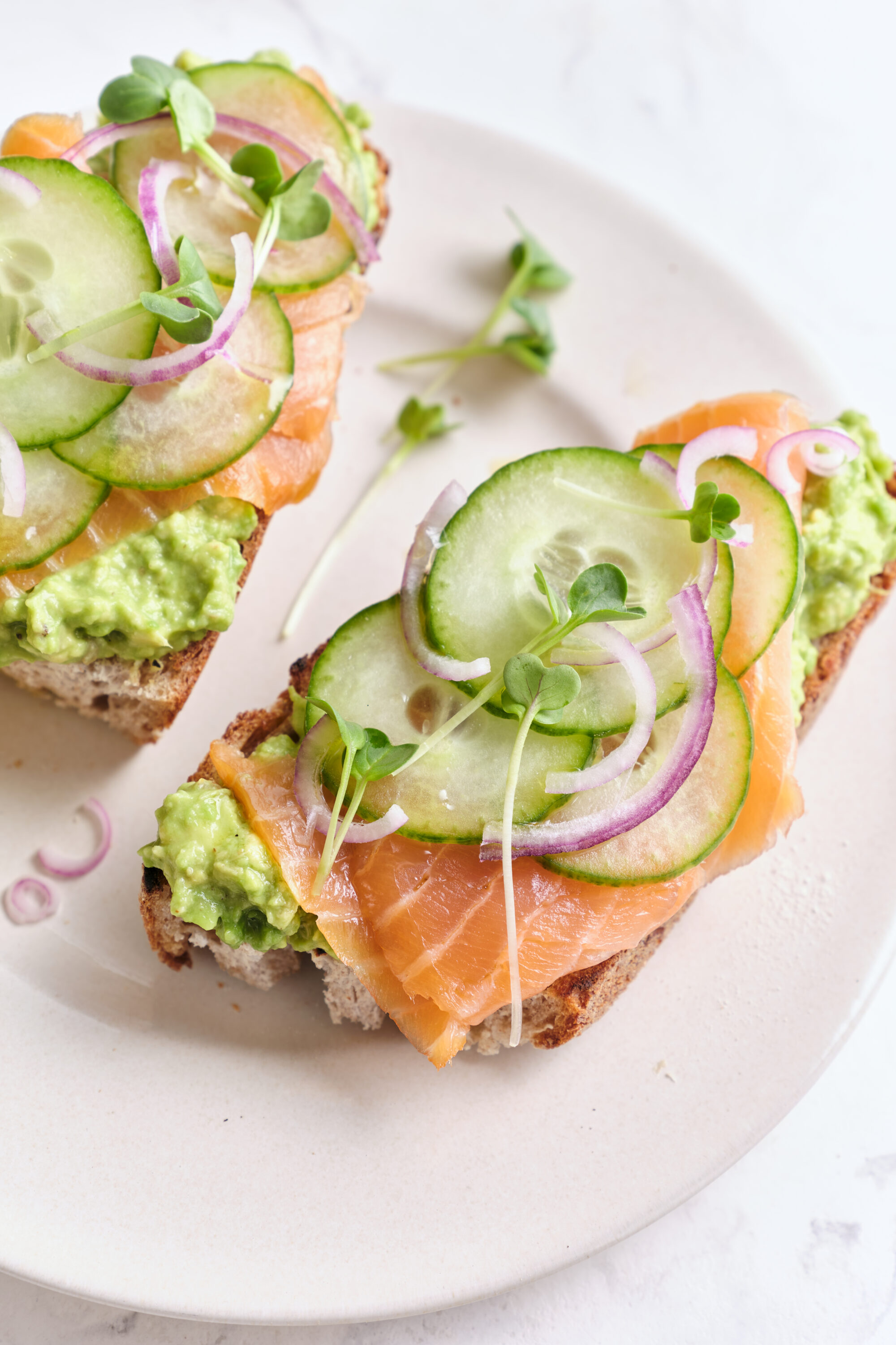 Fresh smoked salmon avocado toast with cucumber, red onion, and microgreens on whole grain bread, healthy and delicious breakfast idea.