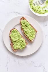 Creamy avocado toast on whole grain bread topped with ripe mashed avocado, served on a white plate, highlighting healthy eating and nutritious breakfast options.