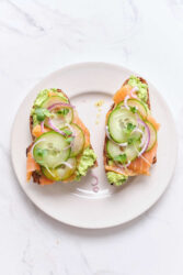 Fresh smoked salmon avocado toast with cucumbers, red onions, and microgreens on whole grain bread, healthy and delicious breakfast option.