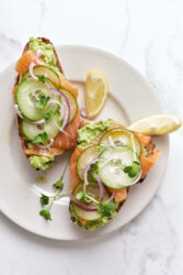 Fresh avocado, smoked salmon, cucumber, red onion, and microgreens on whole grain toast, served with lemon wedges. Healthy, nutritious breakfast or snack options from Food Faith Fitness.