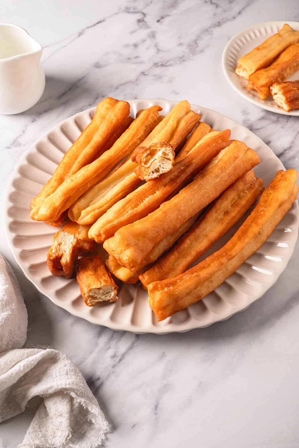 Golden baked churros on a white textured plate, perfect for healthy breakfast or snack recipes from Food Faith Fitness.